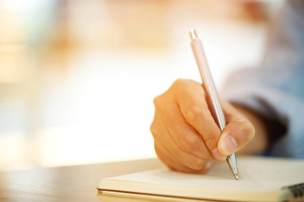 istock close up hand young man are sitting using pen writing Record Lecture note pad into the book on the table wood. 1533608386