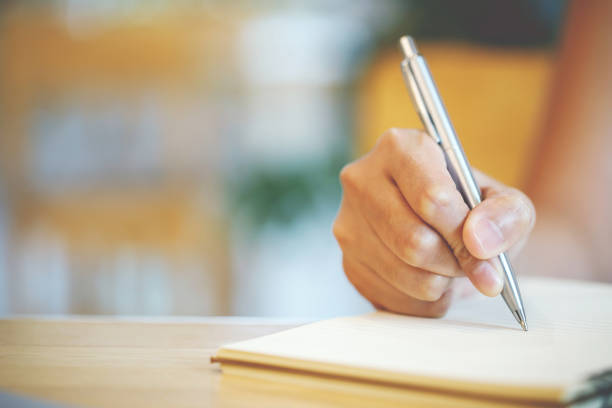 istock close up hand young man are sitting using pen writing Record Lecture note pad into the book on the table wood. 1533611129