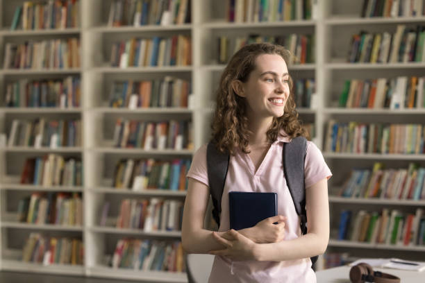 istock Happy dreamy student girl with backpack posing in campus library 1533629142