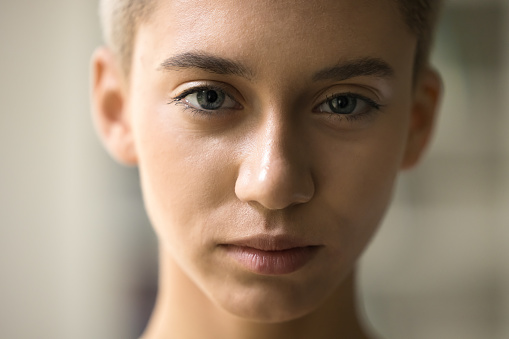 Serious beautiful face of young teenage girl with short haircut, clean smooth skin looking at camera. Pretty teenager, beauty care model cropped close up shot, facial portrait