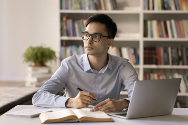 istock Pensive smart student guy in glasses studying in university library 1533630235