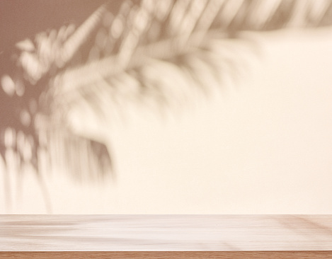 Blurred shadow of tropical palm leaves on beige wall and table top in the foreground. Summer concept.
