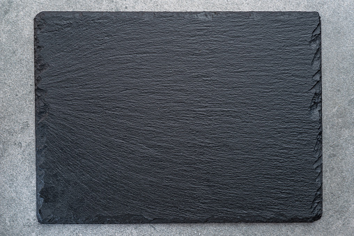 Empty natural stone black slate serving plate on light grey background. Flat lay.