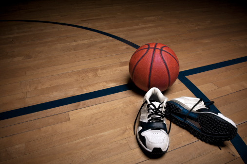 A basketball court floor with a ball and athletic shoes as the focal point