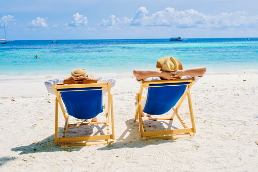 a couple of men and women on beach chairs on the beach of Koh Lipe Island Southern Thailand, with turqouse colored ocean and white sandy beach at Ko Lipe.