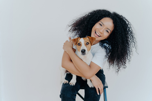 Curly girl smiles, embraces beloved dog, enjoys good time together, showcasing their close relationship.