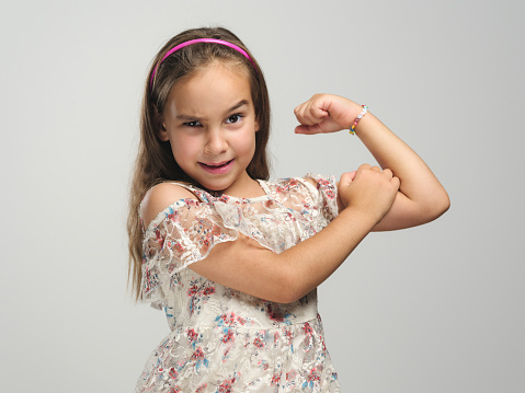 Portrait of a happy child girl showing off her muscles