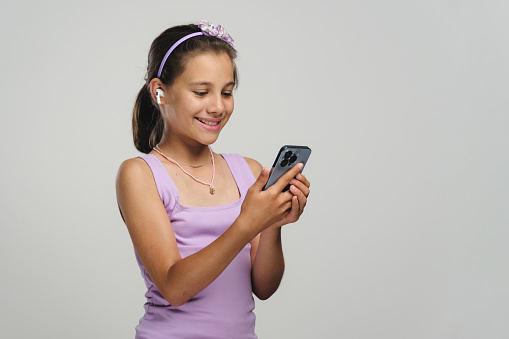 Studio shot portrait of a beautiful child girl using smartphone and wireless earphones, selfie concept