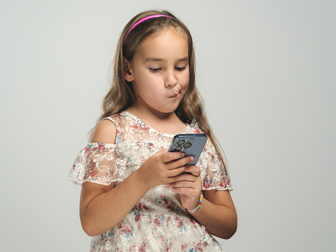 Studio shot portrait of a beautiful child girl using smartphone and wireless earphones, selfie concept