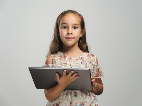 Portrait of a child girl playing video game on digital tablet on grey background