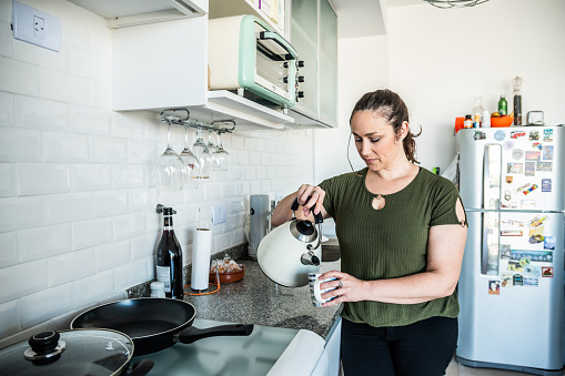 Mature woman pouring tea/water on a mug at kitchen home