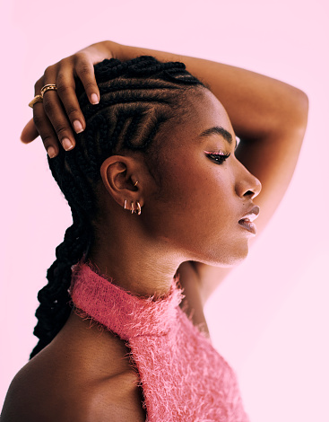 a beautiful black African woman with cornrow protective styling shot against a pink backdrop. Stock photo
