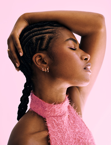 a beautiful black African woman with cornrow protective styling shot against a pink backdrop.