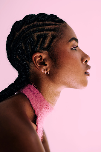 side profile shot of a beautiful African woman with cornrows shot in front of a pink backdrop. Stock photo