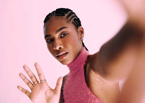 a beautiful and vibrant young black woman holding her hands up towards the camera and dressed in pink posing in front of a pink backdrop. Stock