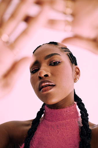 a beautiful young black woman frames her face with her hands while standing in front of a pink backdrop Stock photo