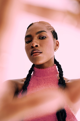 a beautiful young black woman frames her face with her hands while standing in front of a pink backdrop Stock photo