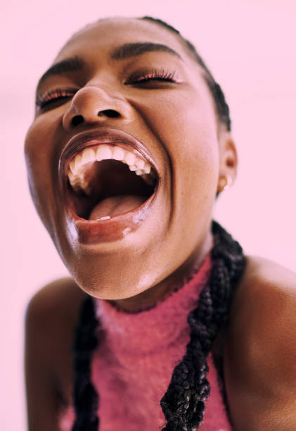 joyful expression . Stock photo Close up shot of a young black woman expressively laughing into camera in front of  a  pink background Stock photo mouth open stock pictures, royalty-free photos & images