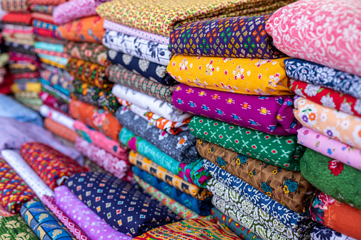 Cotton fabrics. Natural multi-colored fabrics with various patterns and patterns are in large piles in fabric store. Different textures of fabrics. Textile production and sale. Natural bright dyes.