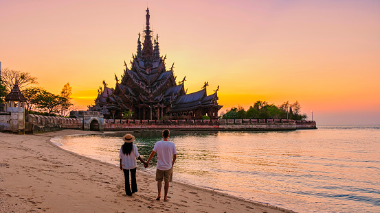 A couple of men and women visit the Sanctuary of Truth, Pattaya, Thailand, wooden temple by the ocean during sunset on the beach of Pattaya.