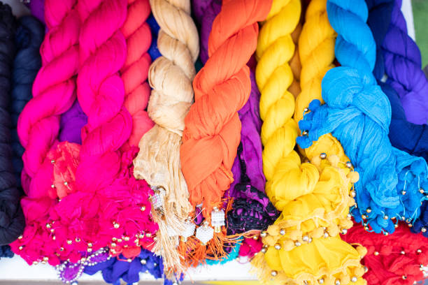 Thin silk, cotton, viscose shawls, scarves and pashmina multicolored with fringe rolled up in rolls are laid out by group in a showcase atmarket. Group of products. Trade, eastern market.