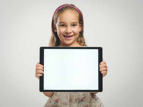 Portrait of a child girl holding digital tablet with white screen, on grey background