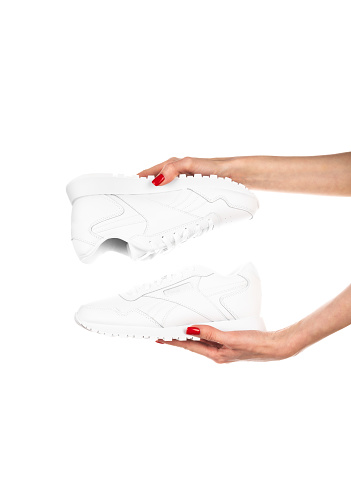 White leather female sneakers in hands isolated on white background. Fashionable stylish sports casual shoes. High quality photo