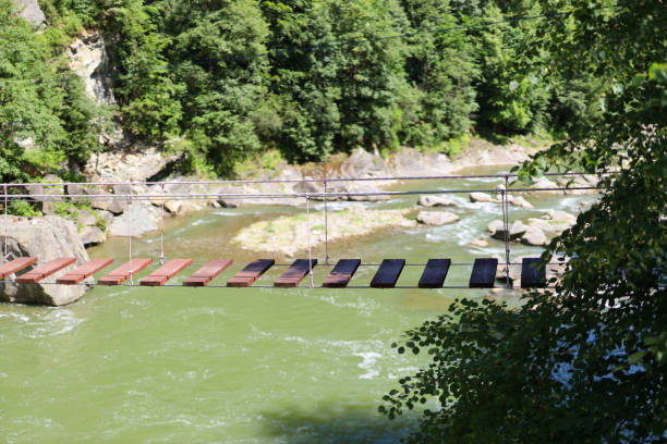 hölzerne hängebrücke über einen gebirgsfluss. - sky blue grass green stock-fotos und bilder
