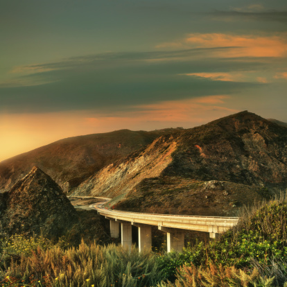 Road and bridge at sunset at the Big Sur coast in Monterey county, California. Long exposure, some motion trails from moving cars.