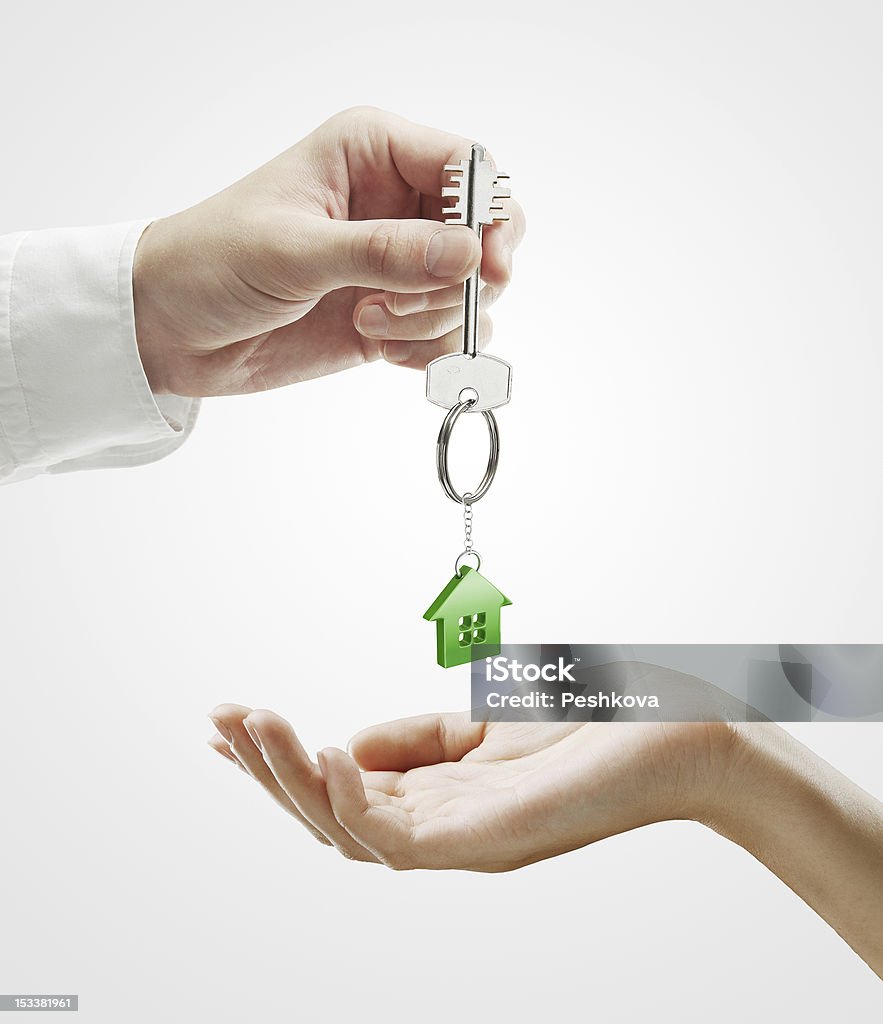 Man is handing a house key to woman Man is handing a house key to woman.Key with a keychain in the shape of the house. On a gray background Adult Stock Photo