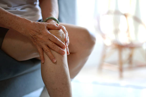 아시아 노인 여성이 집 거실 소파에 앉아 무릎 마사지를 하고 있다 - arthritis senior adult rheumatoid arthritis sadness 뉴스 사진 이미지