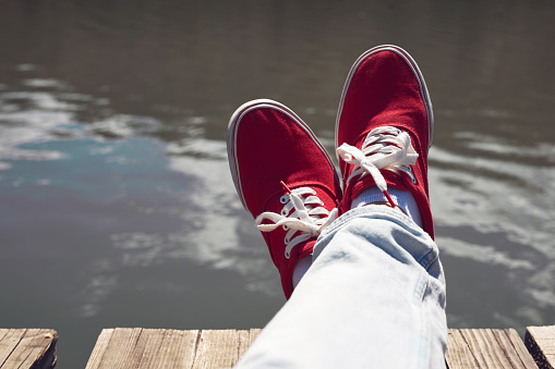 Person in red shoes relaxing on a lake wooden deck.