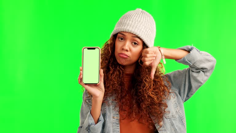 Green screen, thumbs down and woman face with phone mockup and bad review on studio background. Negative, feedback and portrait of sad female person with emoji vote for app, service or connection