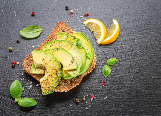 istock Avocado toast - bread with avocado slices on natural slate serving board. Top view. 1533882977