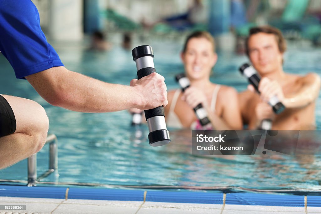Fitness - sports under water in or spa Fitness - a young couple (man and woman) doing sports and gymnastics or water aerobics under water in swimming pool or spa with dumbbells and instructor Underwater Stock Photo