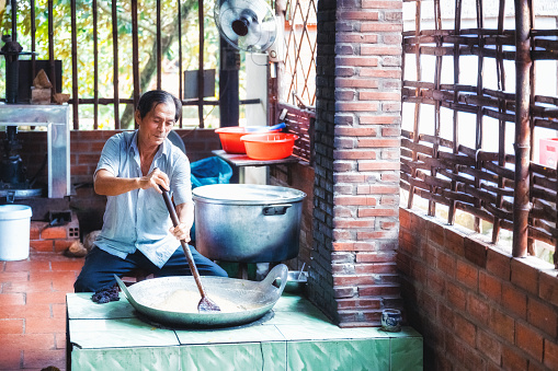 senior man stirring in hot caramel for candy production on open fire in vietnam