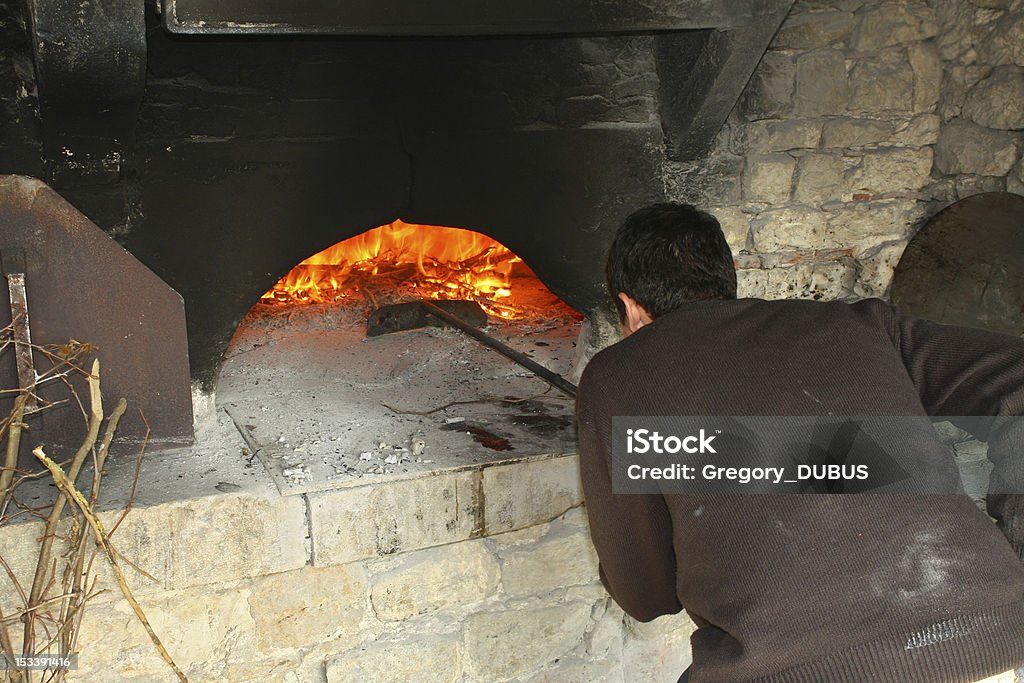 Baker working in oven A man baker scraped the ashes of an old stone oven in working order Adult Stock Photo