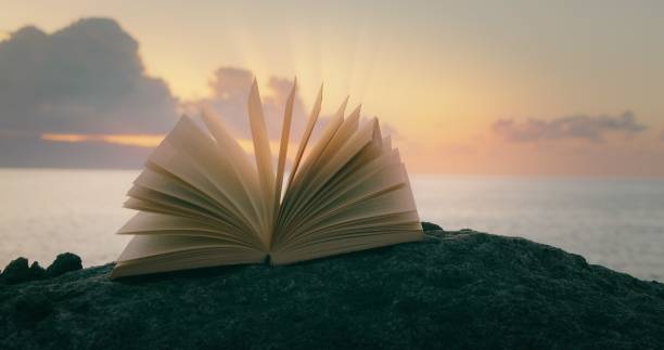 istock Magical glow on pages of open book at sunset. Learning is light and ignorance is darkness. Ancient story on rocky beach. 1533919201