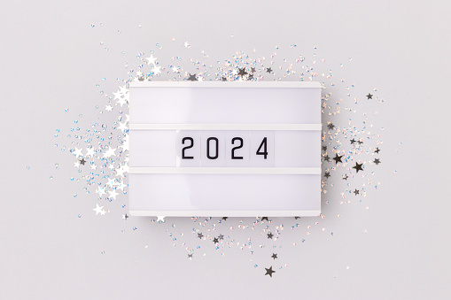 Lightbox with 2024 numbers and glowing silver stars confetti on a blue background. New Year creative concept.