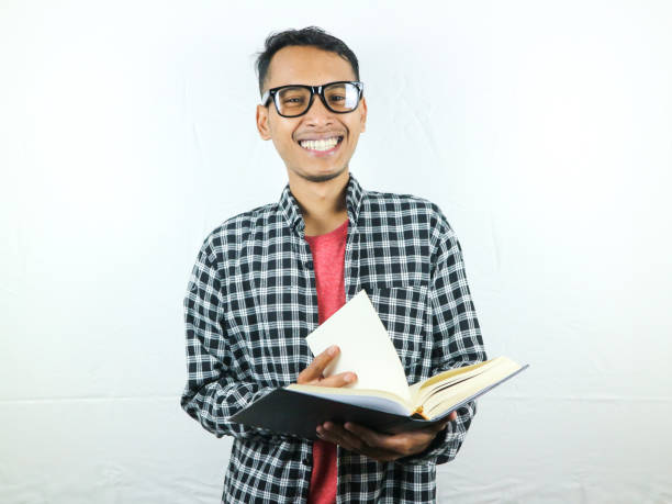 istock Handsome Asian student smiling and holding and reading book in hand 1533954257