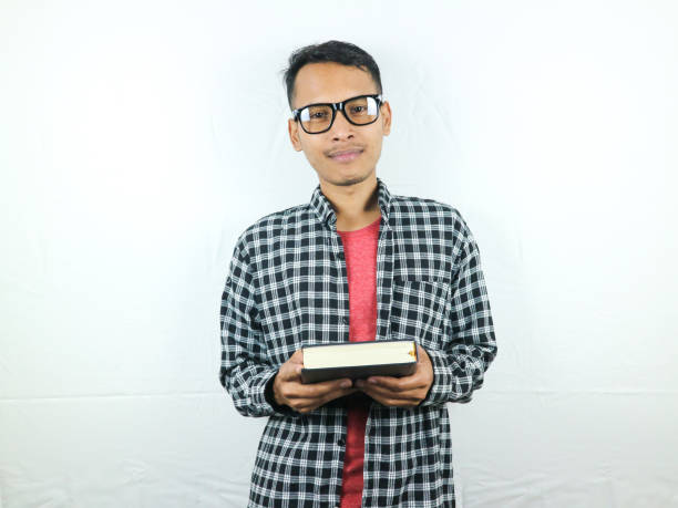 istock Handsome Asian student smiling and holding and reading book in hand 1533954262