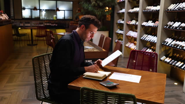 Latin American sommelier using a tablet and notebook planning a wine testing session after closing the restaurant