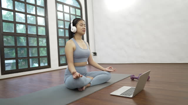 A young woman learning and practicing yoga online with a trainer on laptop to improve physical and mental health.