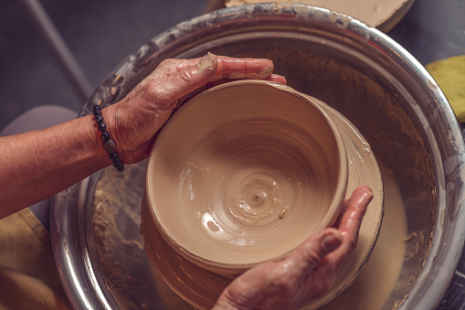 Unrecognizable woman potter creating beautiful plate with clay, making works of art with his hands.