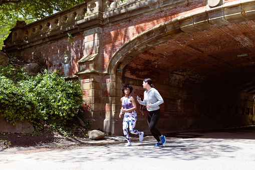 These two active women share a moment of joy as they jog through Central Park, NYC, marveling at the breathtaking skyline that complements their invigorating run. \nFun Fact: Central Park's Great Lawn, spanning 55 acres, is one of the largest open lawns in the city and hosts numerous events, concerts, and picnics!