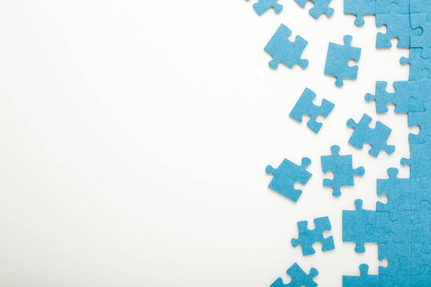 Unfinished blue puzzle pieces on white table background. Closeup. Empty place for text. Top down view. stock photo
