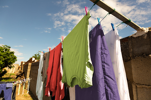 Colorful clothes hanging on some ropes with clothespins, in the courtyard of the village house to air dry on a sunny day with some clouds in the blue sky. Extremadura, Spain.
