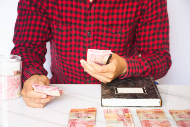 istock Asian man hand counting money Indonesian rupiah and making notes against white background. Making financial plans. Banking and finance, money management, investment concept 1534212147