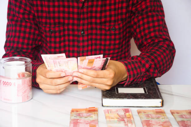 istock Asian man hand counting money Indonesian rupiah and making notes against white background. Making financial plans. Banking and finance, money management, investment concept 1534212687