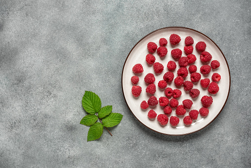 Raspberry in a plate on a gray concrete background. Top view, flat lay, copy space.